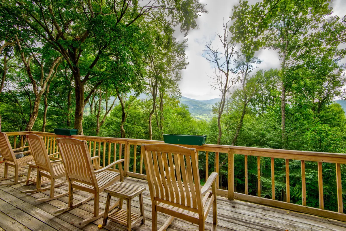 A peaceful outdoor scene with wooden deck chairs overlooking a stunning mountain view, surrounded by green trees. The area is perfect for relaxing, wildlife observation, or stargazing, embodying the year-round appeal of the setting.