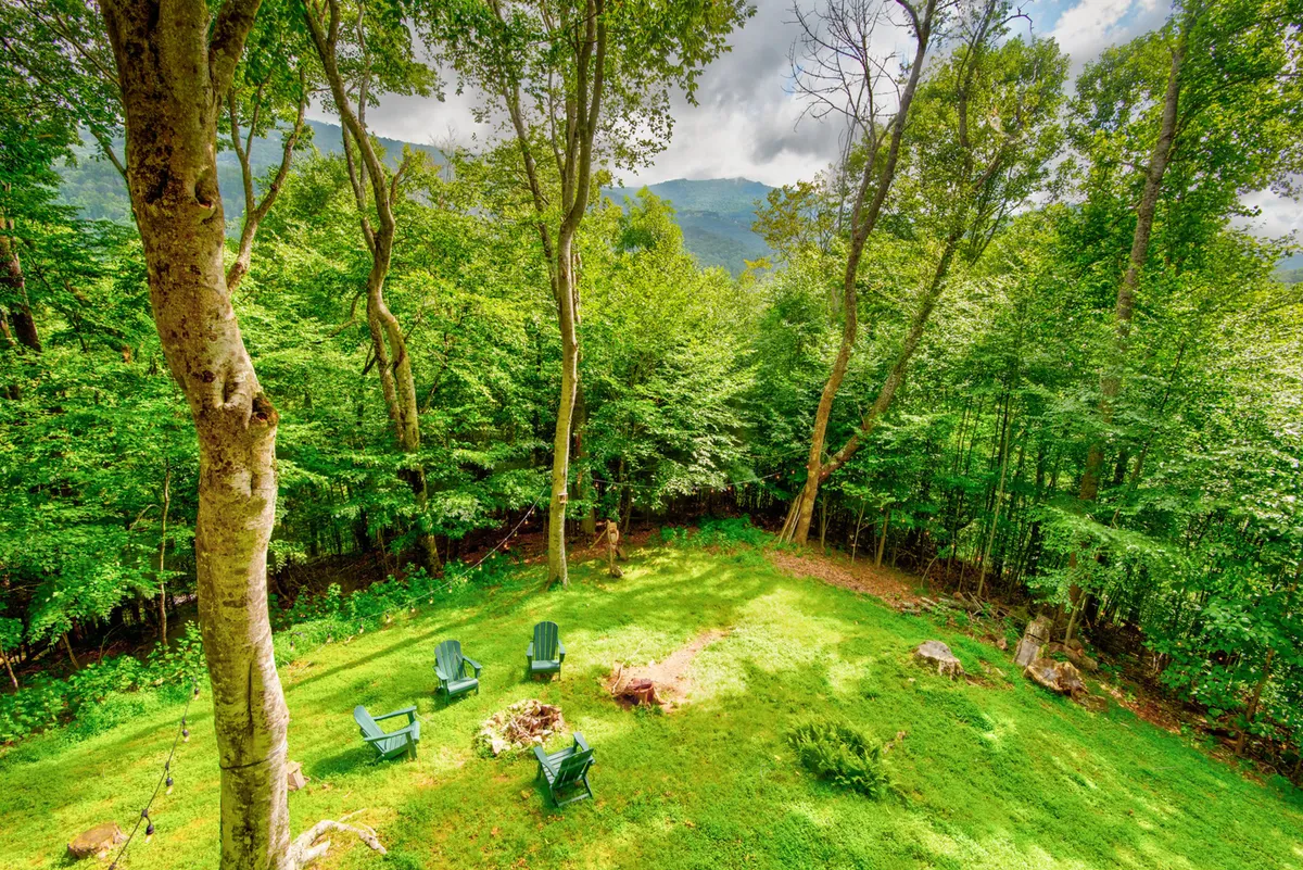 A cozy fire pit area featuring green Adirondack chairs set amidst tall trees, with a stunning view of the mountains in the background. The setup is ideal for campfire gatherings, storytelling, and outdoor fun under the stars.
