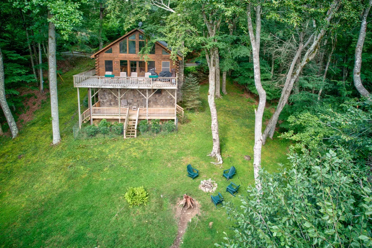An exterior shot of the wooden cabin, showing a deck with chairs, a fire pit, and lush surrounding trees. The view highlights the seamless transition from indoor comfort to outdoor adventure, with plenty of space for pets to explore safely.
