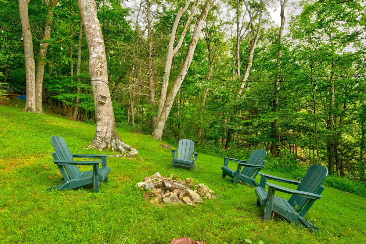 A cozy outdoor fire pit encircled by Adirondack chairs amidst a wooded backdrop, inviting guests to gather and unwind as day transitions to night.